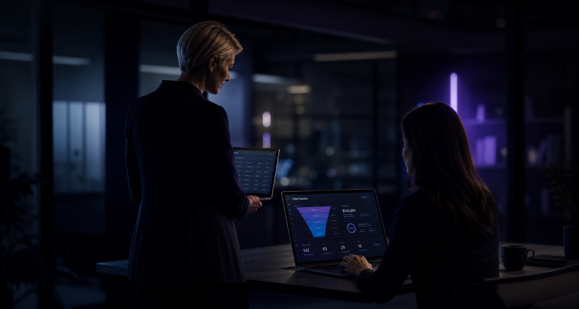 Two consultants reviewing a CRM dashboard together in a modern, dimly lit office